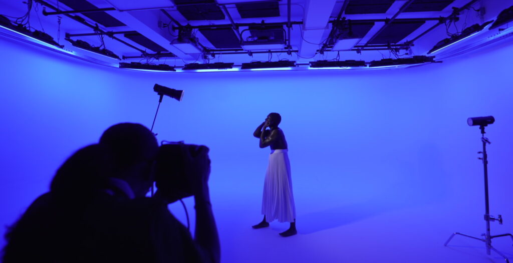 photography studio with full cyc in blue light as subject poses in front of photographer