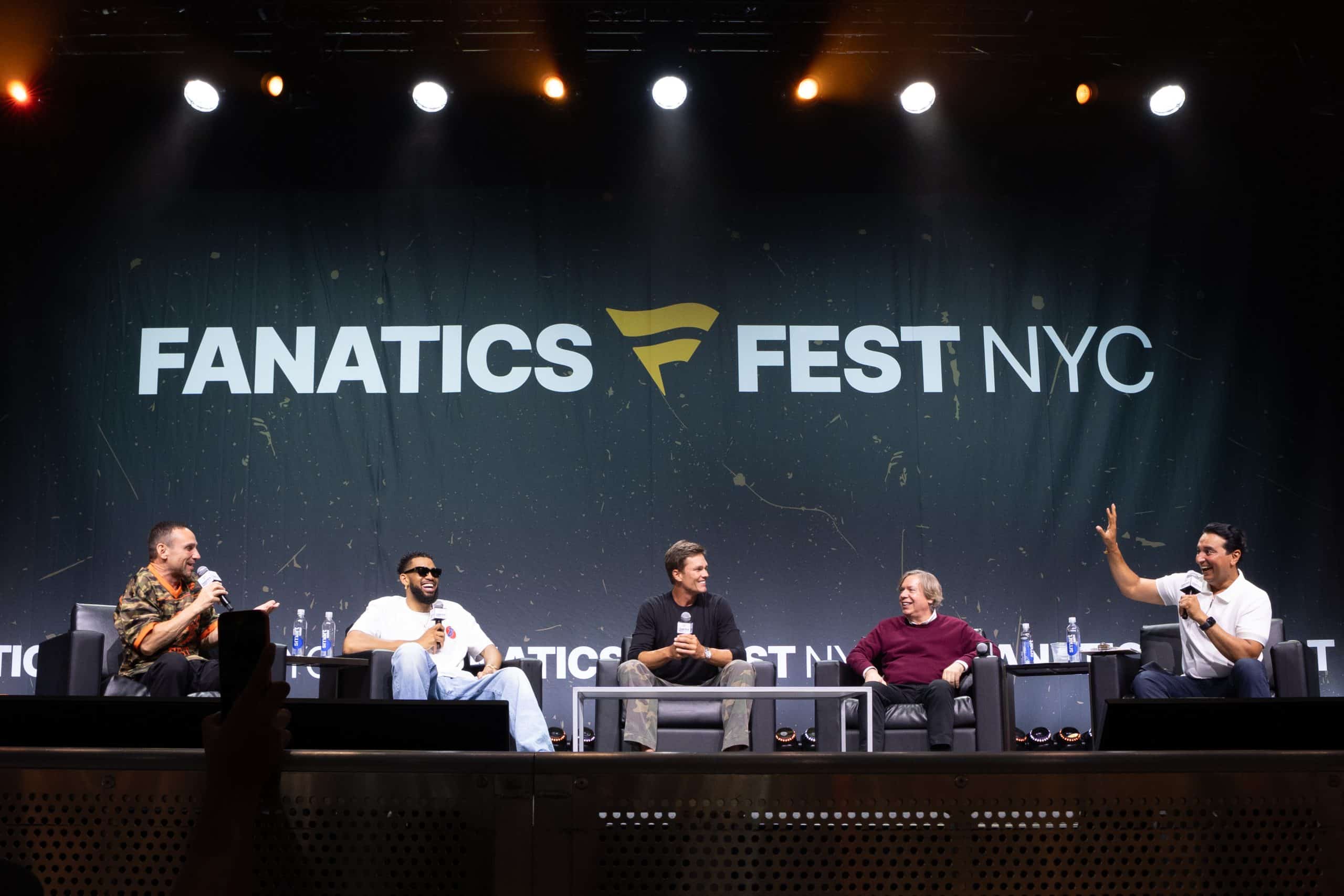 Five men sit on a stage in front of a 