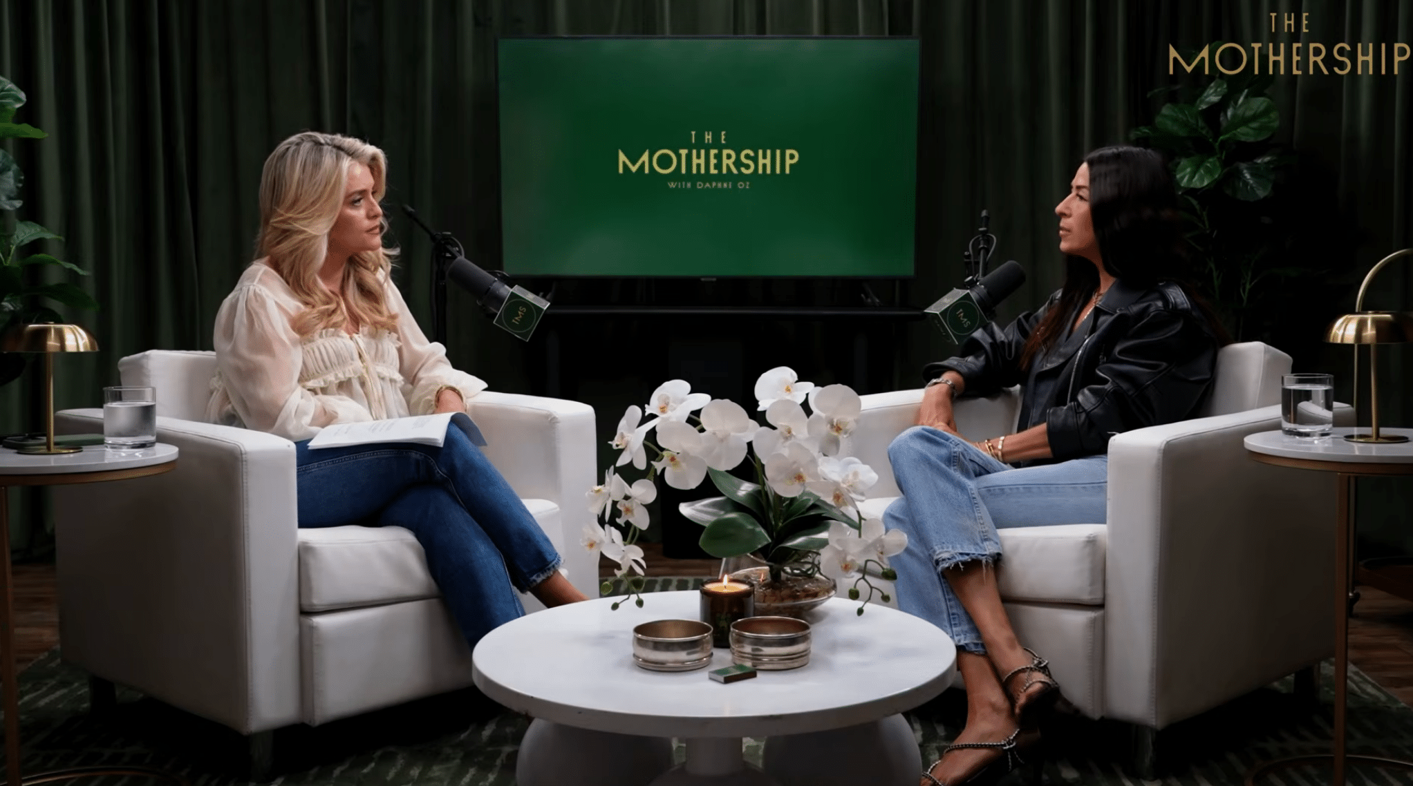 Two women sit in armchairs across from each other for a podcast video production in front of a screen displaying “The Mothership with Daphne Oz” logo.